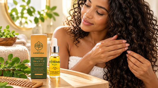Woman applying moringa oil to her long, curly hair, with Zest of Moringa organic oil bottle, product packaging, and fresh moringa leaves displayed on a wooden vanity.